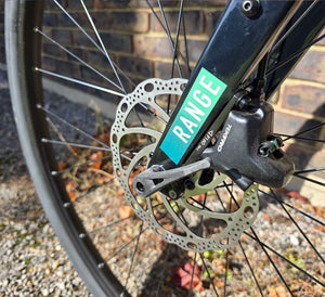 Close-up of a bicycle disc brake with 'RANGE' branding on a brick background