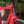 Close-up of a pink bicycle frame with a black vertical section and a white stylised 'K' logo on the head tube, photographed outdoors with blurred green foliage in the background.