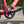 Close-up of a black SRAM Apex bicycle crankset with a chainring and chain, attached to a bright pink road bike frame outdoors.