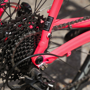 Close-up of a bright red bicycle frame near the rear cassette and chainring, with a small black-and-white 'K' logo transfer on the seat tube.