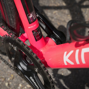 Close-up of a bright pink bicycle frame with visible SRAM and KINESIS branding, showing part of the crankset and seat-tube against an outdoor pavement background.