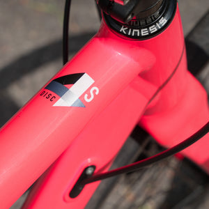Close-up of a bright pink bicycle frame with a visible 4S Disc logo decal and part of a Kinesis stem, photographed outdoors on pavement.