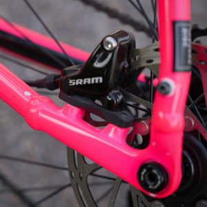 Close-up of a bright pink bicycle frame with a black SRAM brake mech attached near the rear wheel.