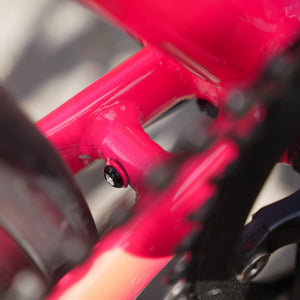 Close-up of a bright pink bicycle frame with a black chainring and cassette visible in the foreground.