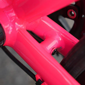 Close-up of a bright neon pink bicycle frame with glossy finish, showing structural tubing and a black cable running through the frame.