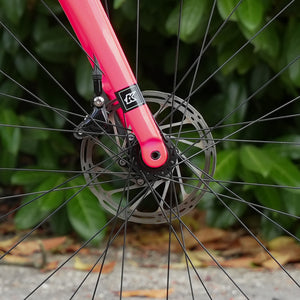 Kinesis 4S pink fork and front dis brake against blurred foliage background
