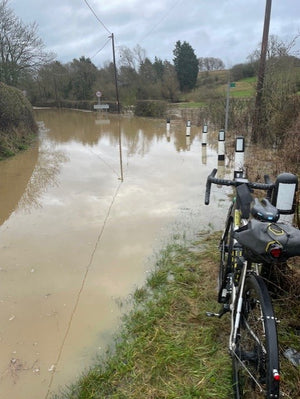 Bicycle leaning against a flooded road with water covering the pavement and surrounding area.