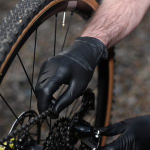 Person wearing black mamba gloves adjusting a bicycle chain.