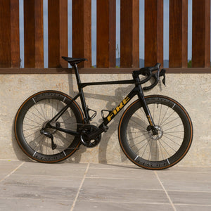 A fire branded road bike leaning against a wall with wooden pillars above and complete with Boyd Cycling 55mm SL Carbon Road wheels