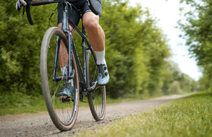 Person cycling on a dirt gravel path with greenery in the background, Kinesis G2 bike
