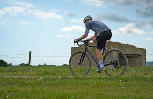 Person riding a Kinesis G2 gravel bicycle in an open field with a clear sky