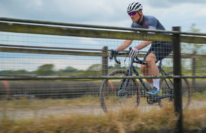 Cyclist riding a bike along a fence in an open field, Kinesis G2 gravel bike