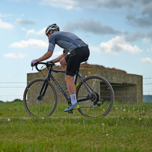 Cyclist riding a bicycle on a gravel patrh by a grassy field with a clear sky.