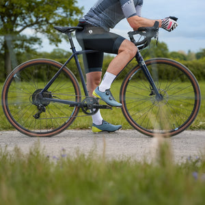 Person riding a bicycle on a gravel path with greenery in the background