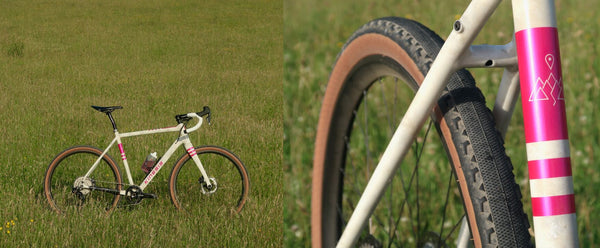 A close-up of a Kinesis Tripster bicycle frame and front wheel with a pink and white frame, shown alongside a full view of the bicycle in a grassy field.