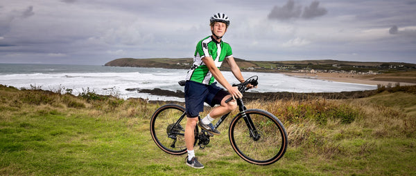 Kinesis Ambassador Joshua Moodie on is Tripster AT Plus next to a scenic sea wall with the waves breaking behind him.