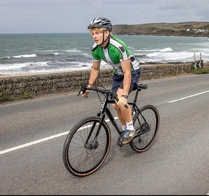 Kinesis Ambassador Joshua Moodie on is Tripster AT Plus riding along a road next to a sea wall with the waves breaking behind him.