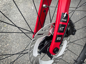 Close-up of a bicycle's disc brake system with a red caliper and 'K' branding.
