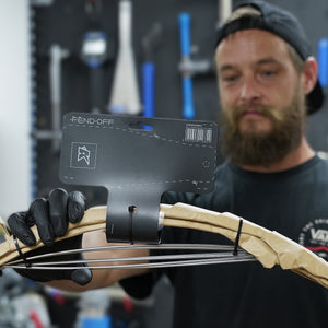 A man in a workshop holds a bicycle Fend Off mudguard in a beige paper-wrapping and a black hang tag that reads 'FEND-OFF'.