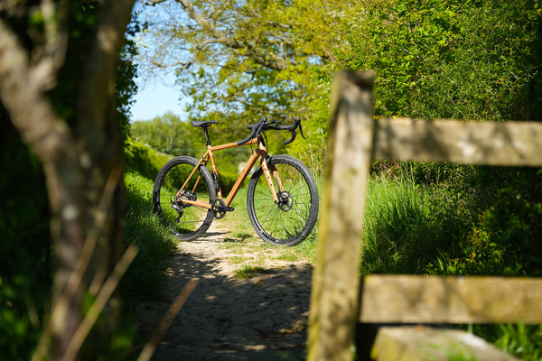Gravel bicycle on a dirt path with greenery and a wooden fence in the background