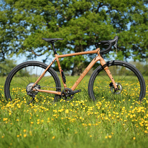 Kinesis Tripster AT full bike build on a grassy field with yellow flowers and trees in the background