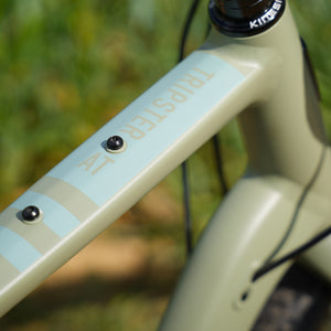 Close-up of a bicycle frame with 'Kinesis' branding against a blurred green background