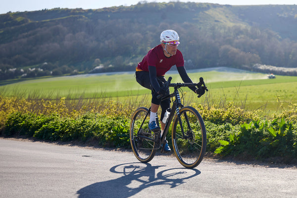 Cyclist riding on a road with green fields and hills in the background