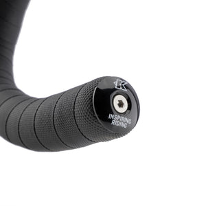 Close-up of a black bicycle handlebar grip tape with a black end cap featuring a silver hex socket and the text 'INSPIRING RIDING' and a stylized 'K' logo, on a white background.