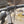 Close-up of a bicycle handlebar with a Ritchey brand black stem and bar-end saddle, mounted on a silver frame with black cables, photographed outdoors with a blurred natural background.