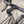 Close-up of a bicycle handlebar and stem assembly, showing black drop handlebars with textured grips, a black stem and headset, and part of a silver metallic frame against an outdoor blurred background.