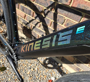 Close-up of a bicycle frame with 'Kinesis' branding against a brick wall.