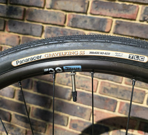 Bicycle tyre with Panaracer GravelKing SS branding against a brick wall background