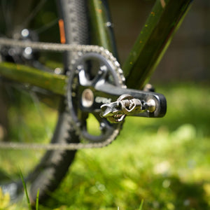 Close-up of Scott's GX Race bicycle pedal and chain with a blurred green background