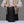 A person wearing a beige vest and light sweater holds open a Wholegrain Cycles black waterproof stuff sack with yellow zipper pulls, standing behind a white table against a grey background.