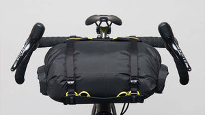 A Wholegrain Cycles Carrie Rack and bag attached to a gravel bike's handlebars and secured with straps and yellow bungees, front on view.