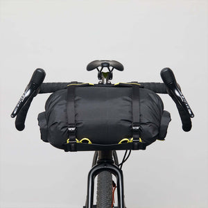 A Wholegrain Cycles Carrie Rack and bag attached to a gravel bike's handlebars and secured with straps and yellow bungees, front on view.