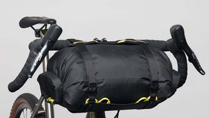 A Wholegrain Cycles Carrie rack and bag mounted to a gravel bike's handlebars and secured with straps and yellow bungees.