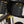 Close-up of a black WHOLEGRAIN bicycle handlebar bag mounted on a dark metallic road bike frame, secured with yellow bungee cords.