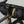 A close-up of a black Wholegrain Cycles Carrie bicycle handlebar bag mounted over the handlebars, secured with black straps and yellow drawstrings, on a grey bicycle against a light grey background.