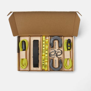 An open cardboard box displaying a set of accessories that come with your Wholegrain Cycles Jack Black bike rack, including bright yellow-green belting, a black webbing strap, gray and black spacers, all neatly organised in individual compartments.