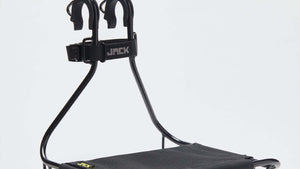 A black Wholegrain Cycle Jack bicycle rack with a padded support and two upright mounting arms, shown on a clean light gray studio background. The brand name 'JACK' is visible on the strap and small yellow logo on the seat.