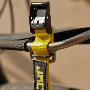 Close-up of a yellow Wholegrain Cycles Stiff strap with a black plastic quick-release buckle and a black fabric label printed with yellow letters, attached to a metal handlebar.